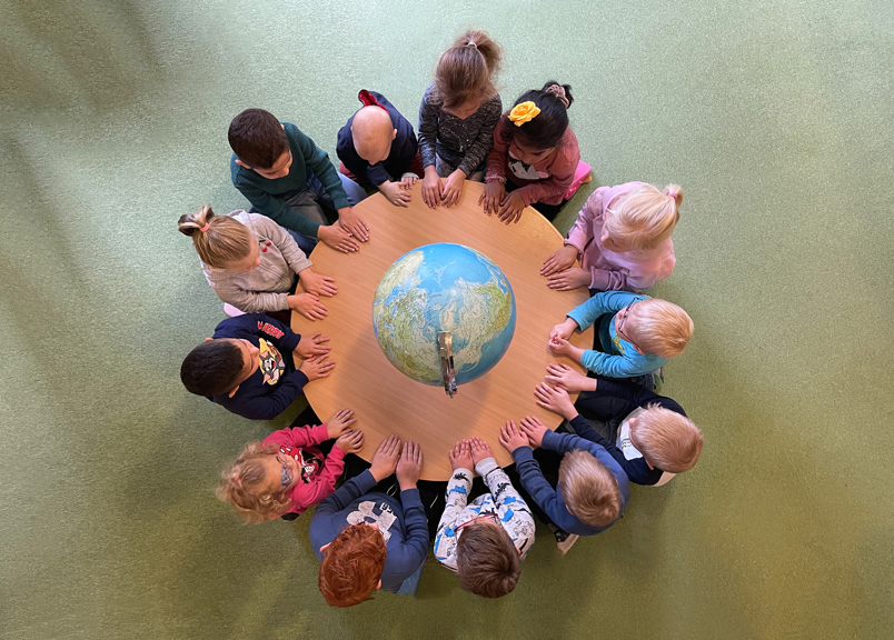 Kinder sitzen an einem Tisch um eine Weltkugel